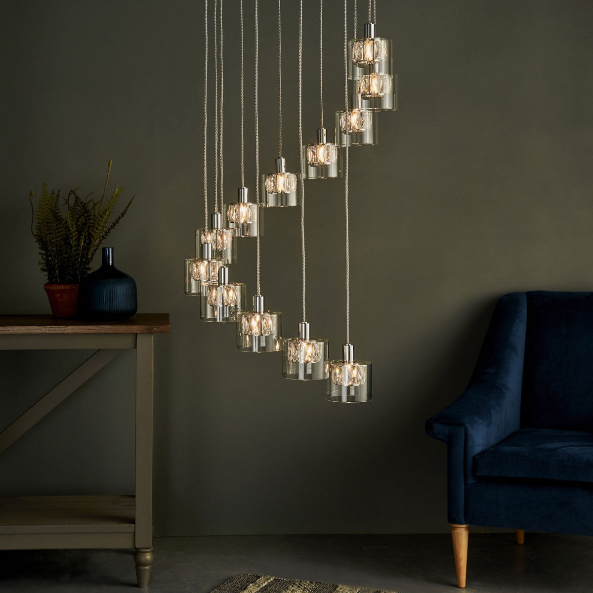 A spiral chandelier with 12 lights, clear glass shades, and polished chrome accents, in a room with a dark wall.