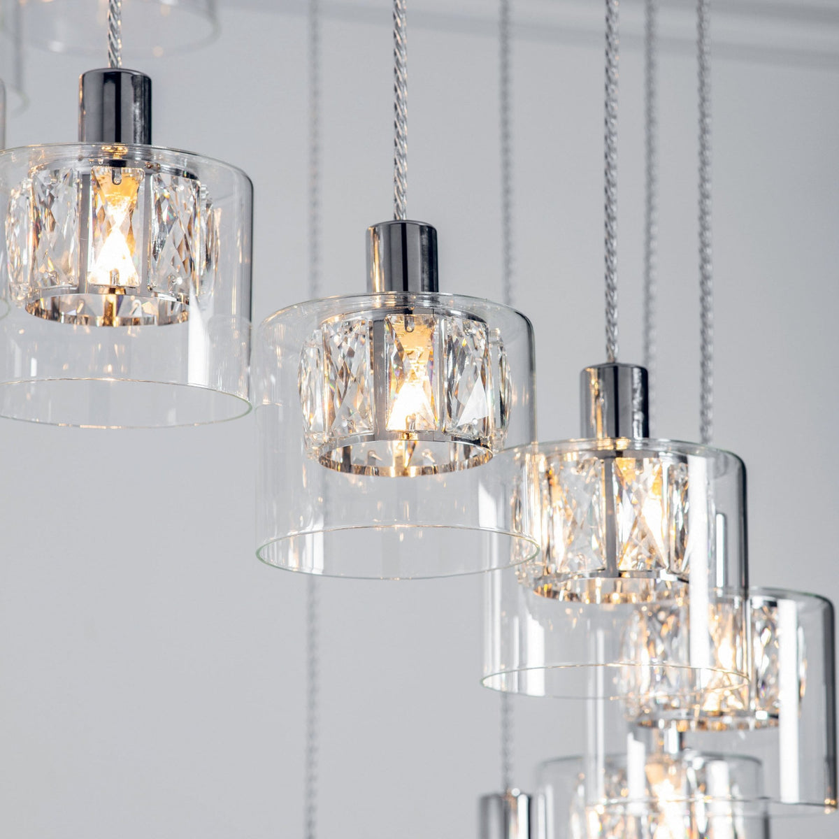 Close-up of three chandelier lights with clear glass shades and faceted crystal inserts, glowing warmly.