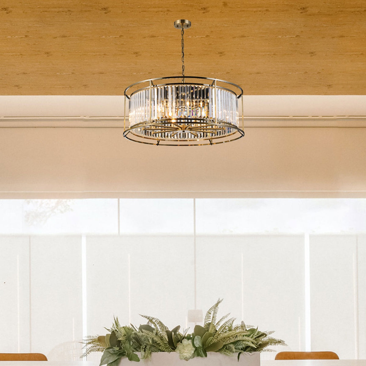 Round crystal chandelier hanging above a dining table with a green plant centerpiece.
