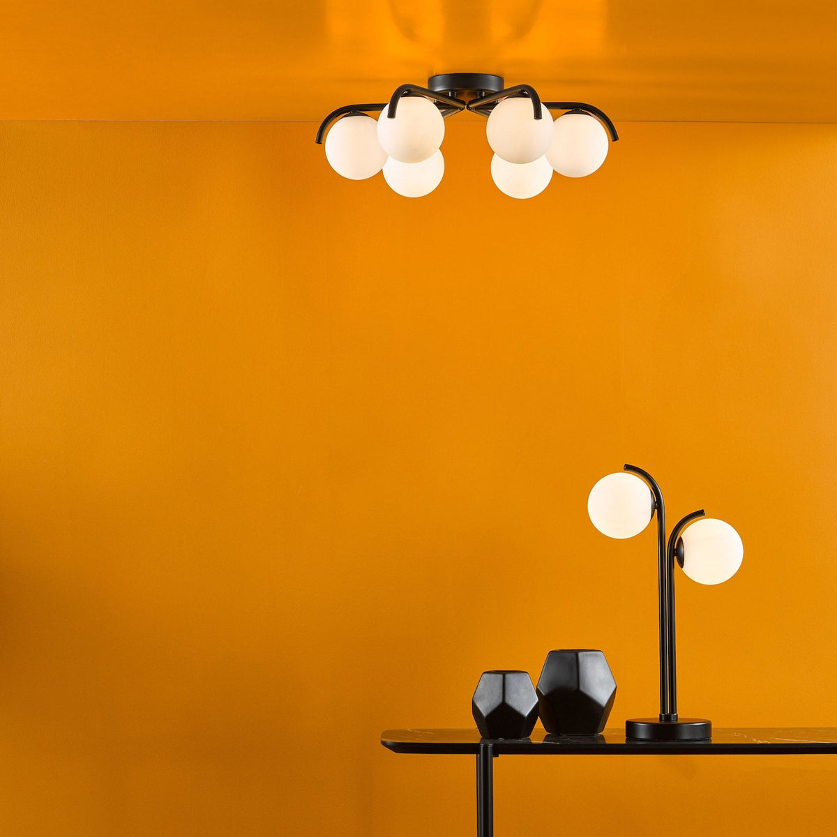 Modern black and white ceiling light and table lamp on a black table with two black vases.