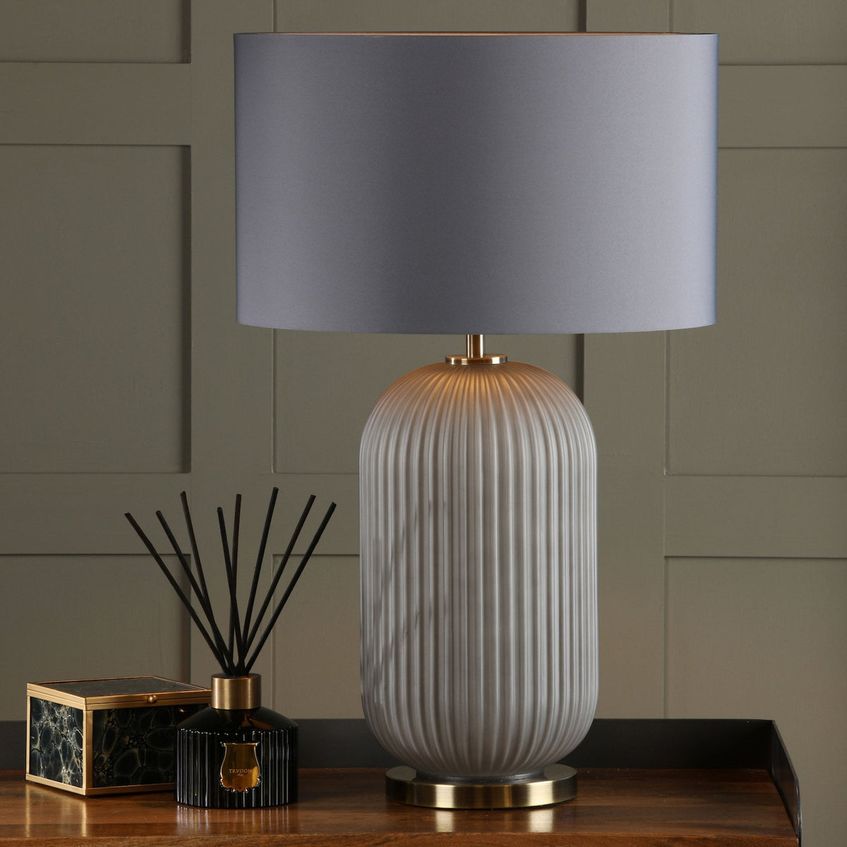 Fluted white ceramic table lamp with a gray shade, next to a black diffuser and a marble box.