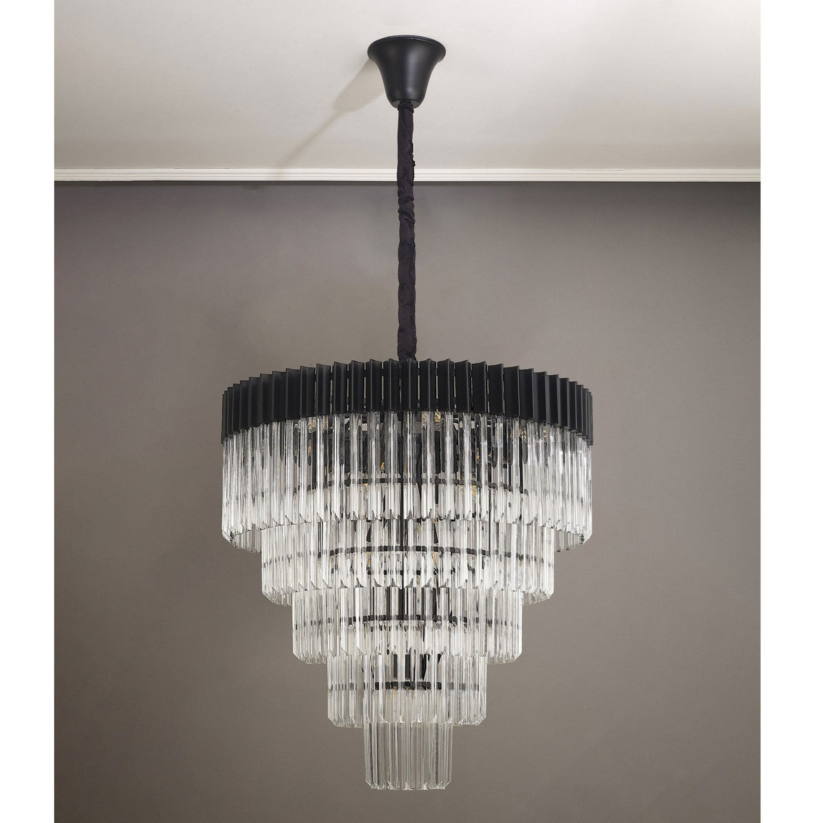 An unlit tiered chandelier with a black frame and clear fluted glass rods hanging in a room.