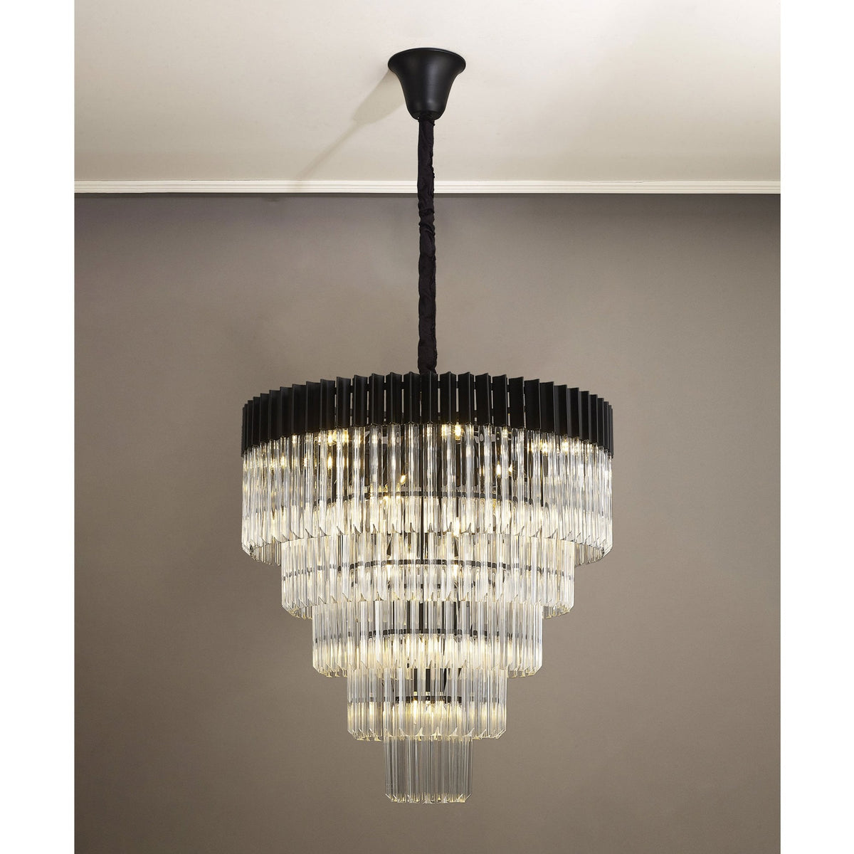 A lit tiered chandelier with a black frame and clear fluted glass rods hanging in a room.
