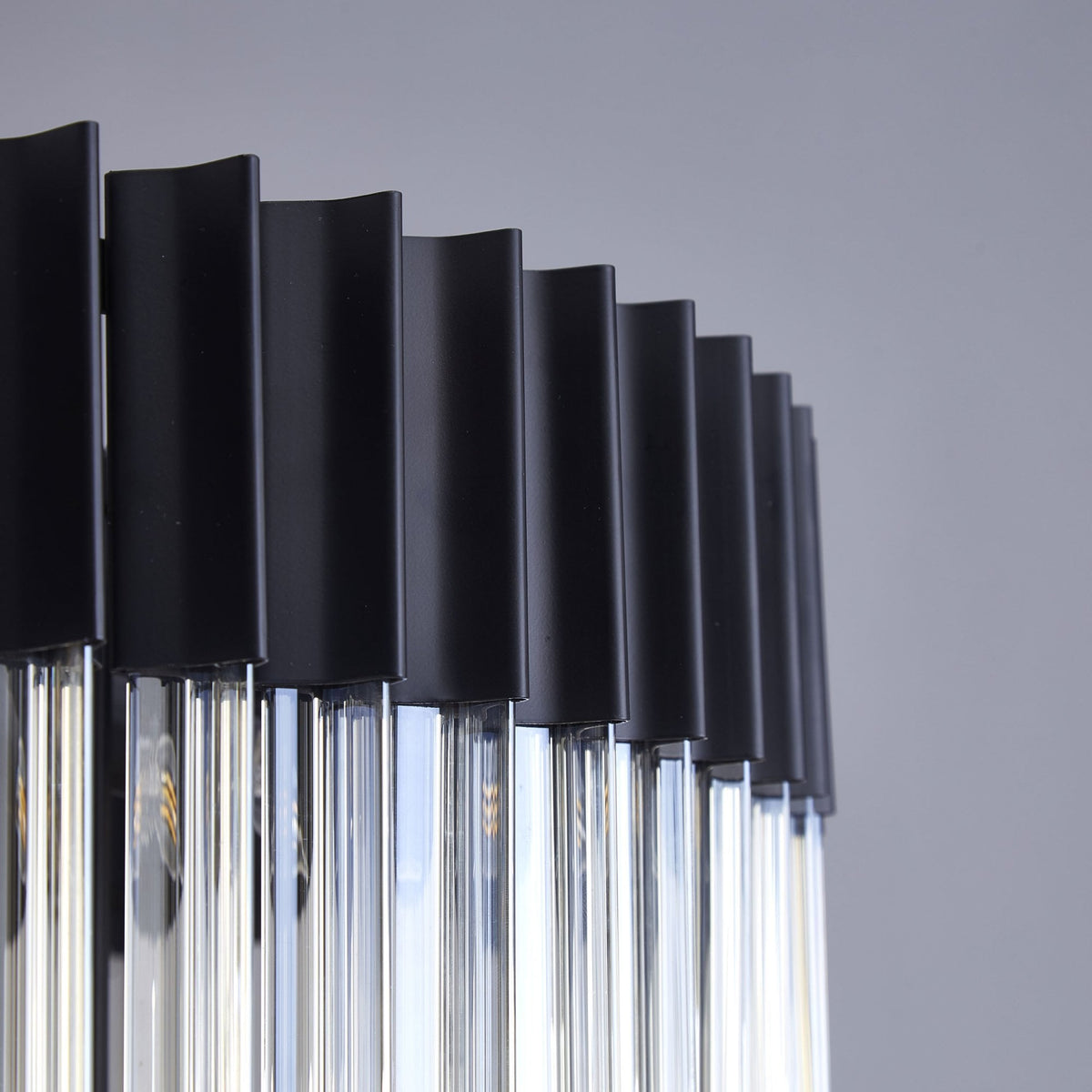 Close-up of the upper section of a chandelier, showing the black frame and clear fluted glass rods.