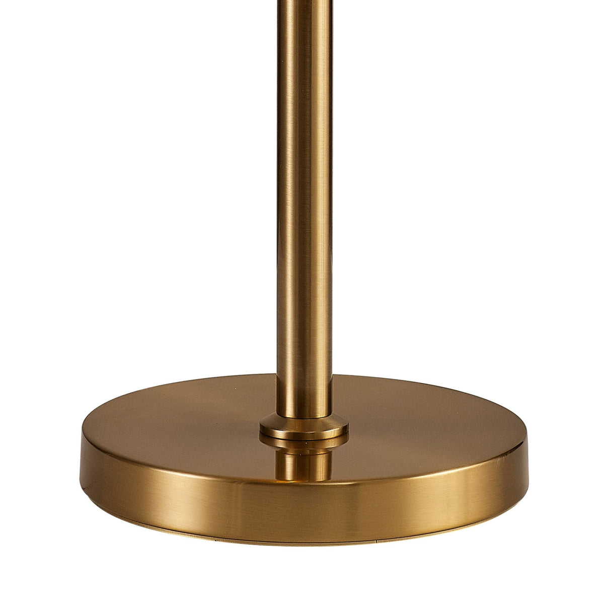A close-up of the circular brass base and slender stem of the modern table lamp.