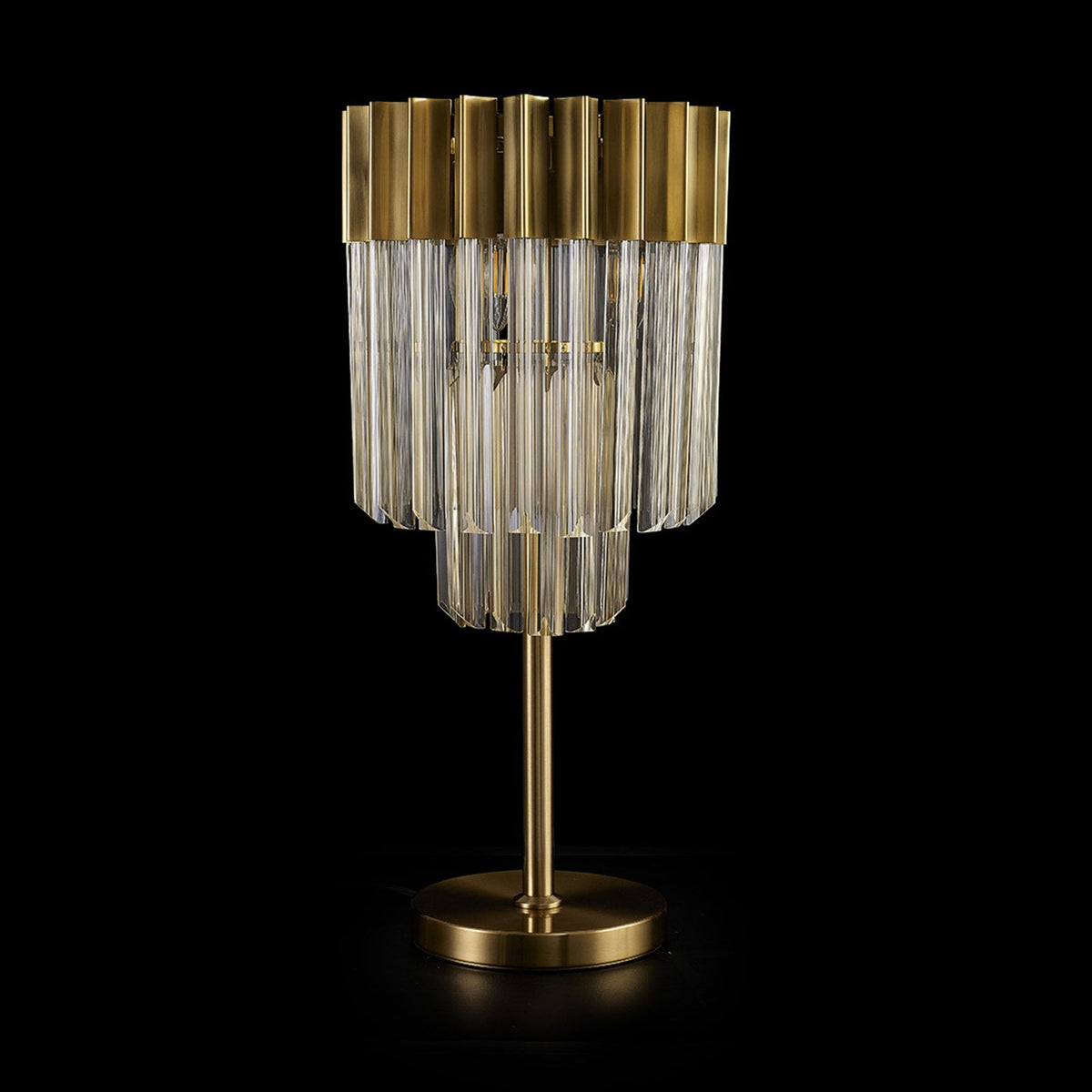 An unlit modern brass table lamp with glass rods on a dark background.