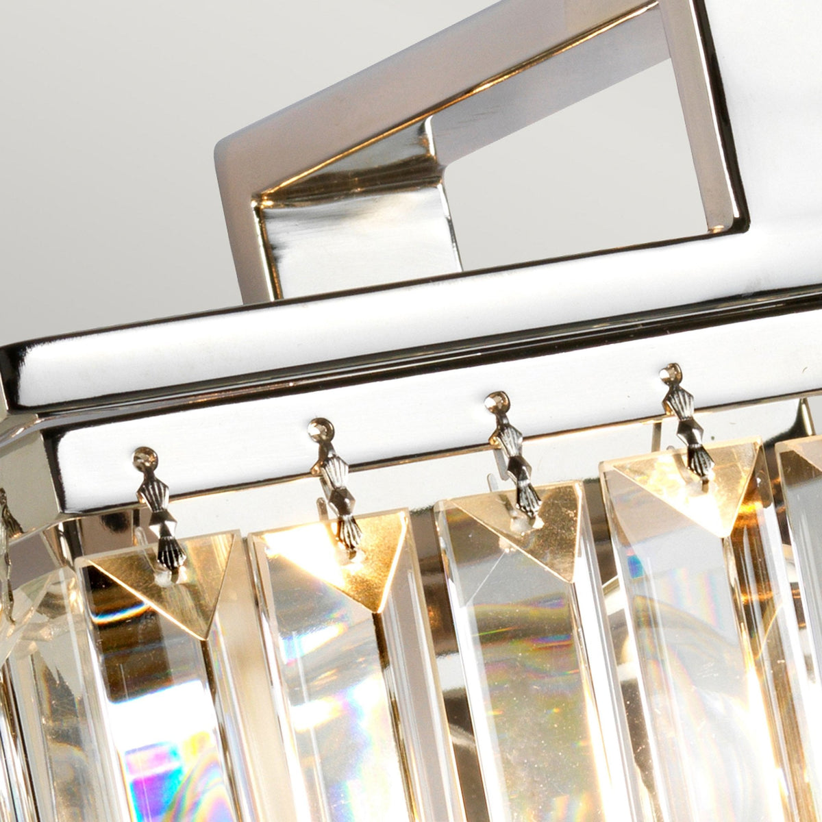 A close-up view of the top chrome fitting and hanging mechanism of a crystal wall light.