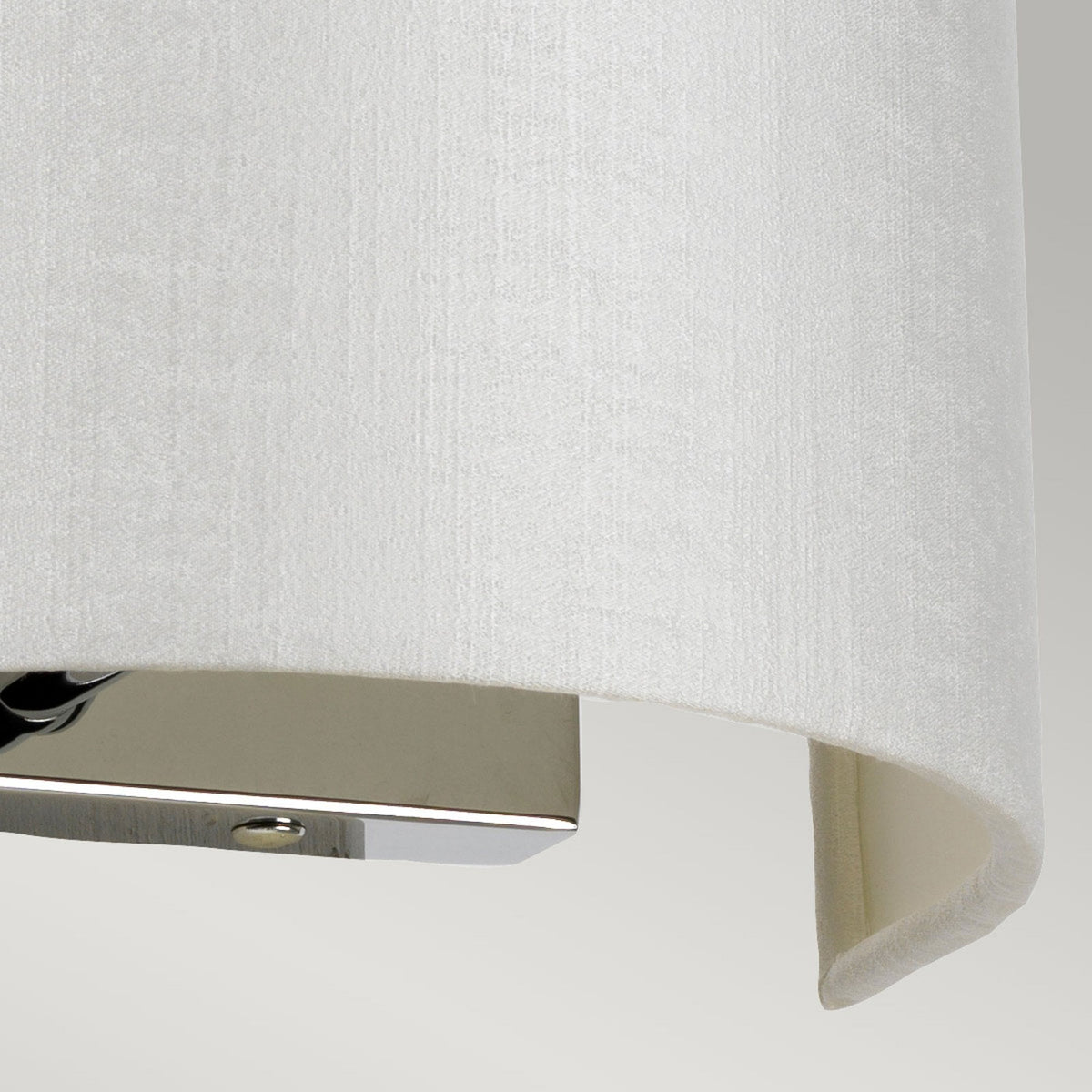 Close-up of the polished chrome base and textured white fabric shade of a wall light.