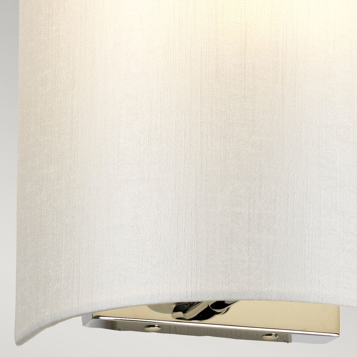 Detail of the illuminated white fabric shade and reflective chrome fitting of a wall light.