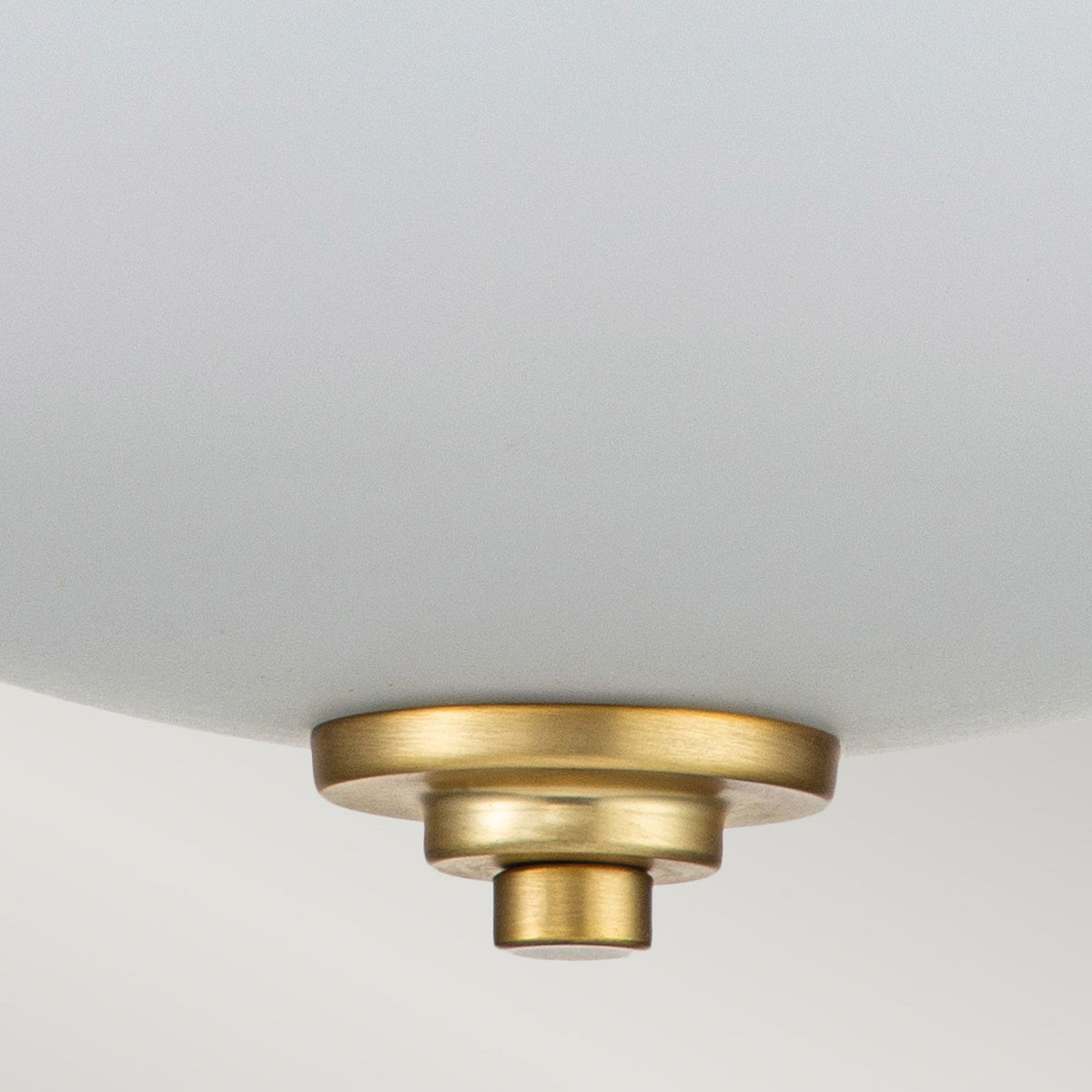 A close-up of the antique brass finial and white glass diffuser of the Capulet flush mount light.