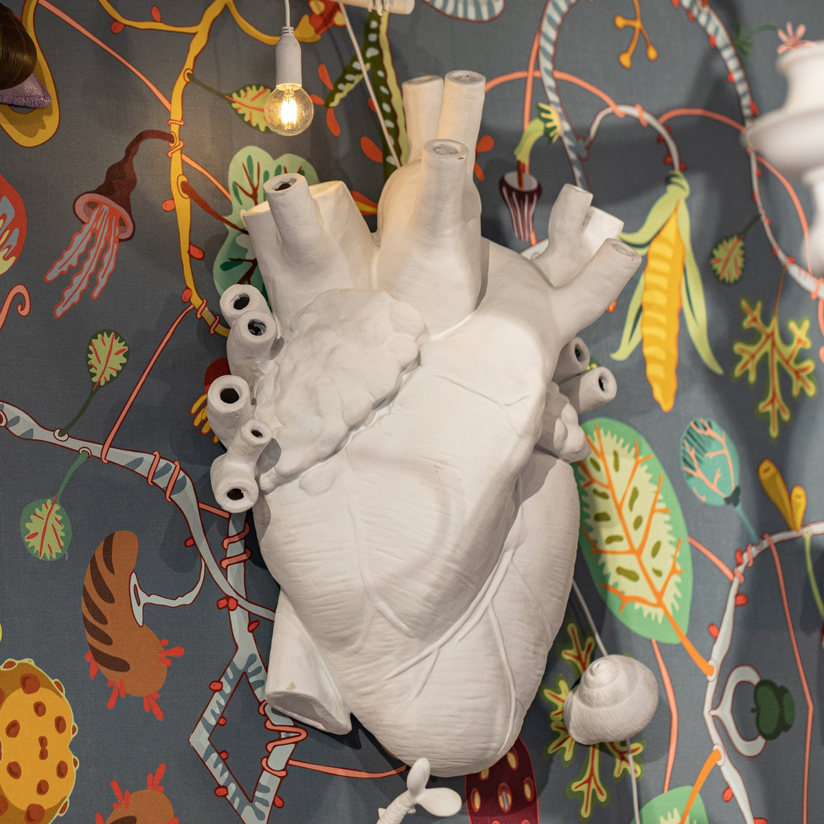 White anatomical heart lamp displayed against a colourful, patterned wallpaper.