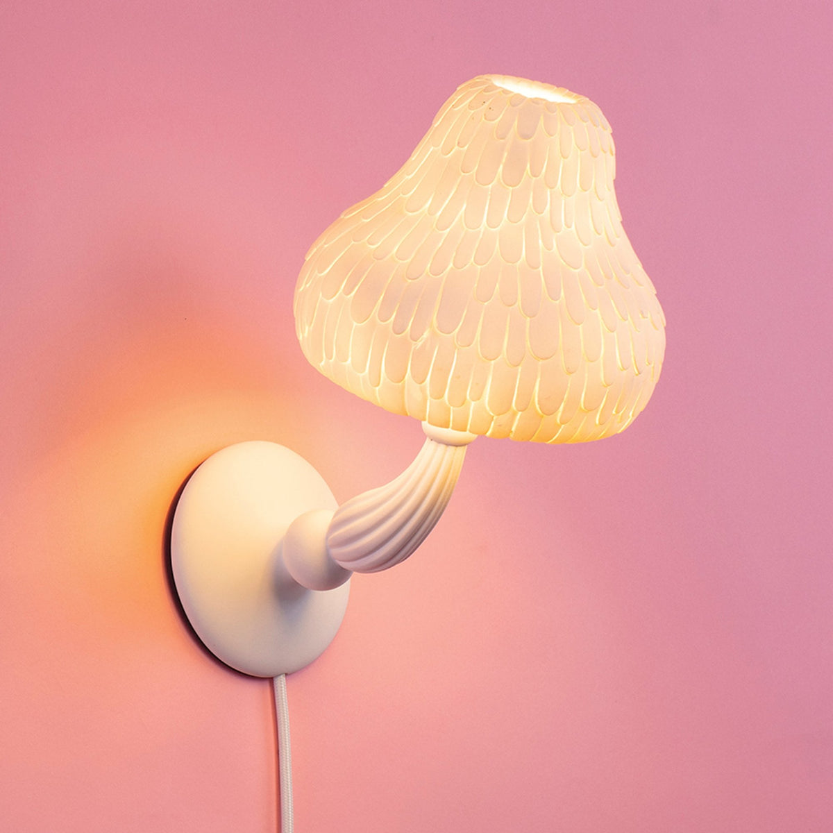 A white mushroom-shaped wall lamp with textured shade glowing on a pink wall.