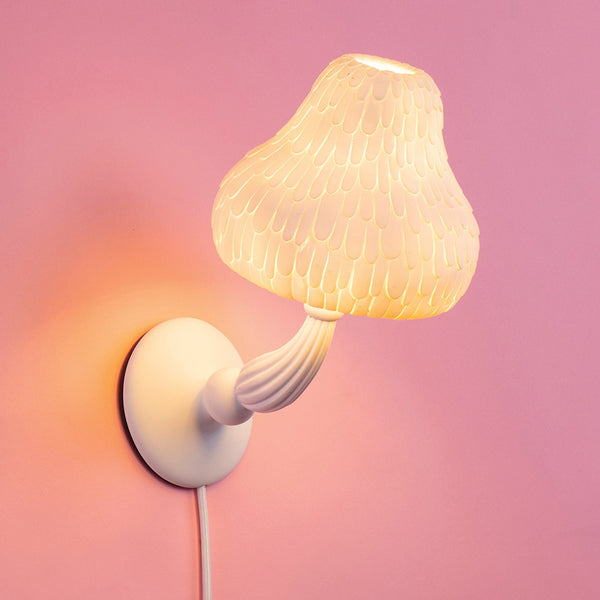 A white mushroom-shaped wall lamp with textured shade glowing on a pink wall.