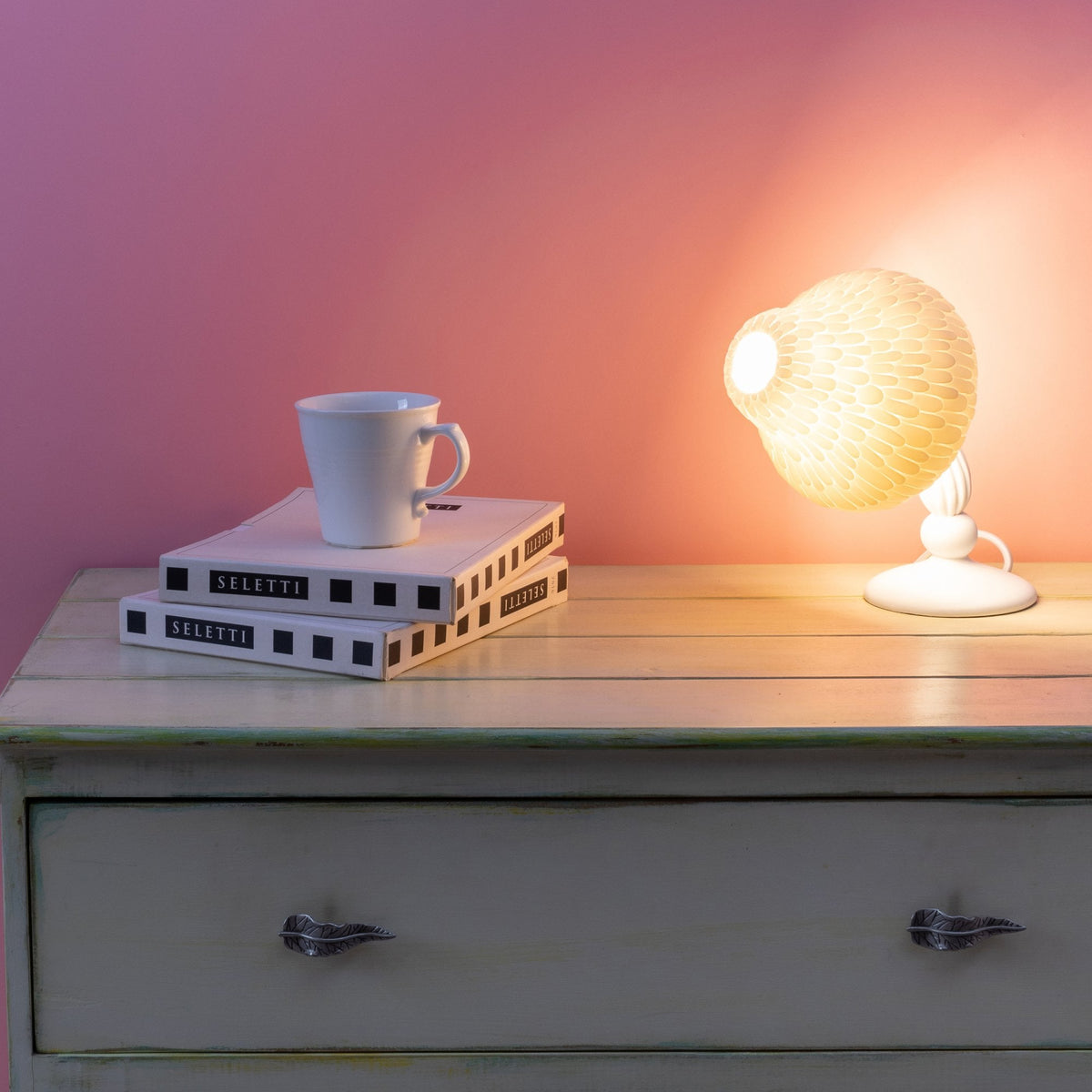 A mushroom-shaped desk lamp illuminates a white mug and stacked books on a wooden dresser.