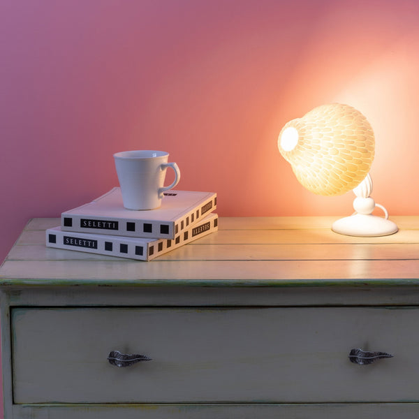 A mushroom-shaped desk lamp illuminates a white mug and stacked books on a wooden dresser.