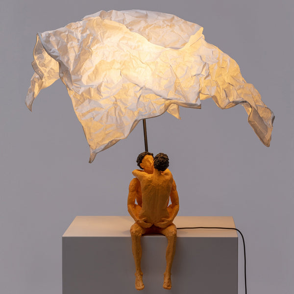 A modern art lamp with a couple embracing under a white crumpled shade, casting a warm glow.