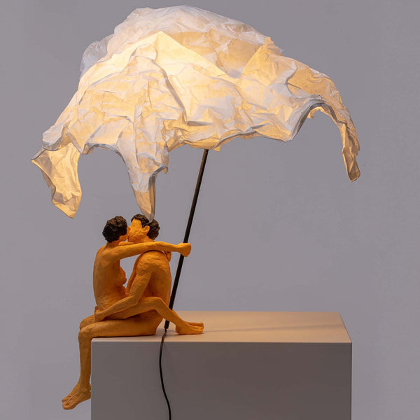 A modern art lamp with a couple kissing under a white crumpled shade, casting a warm glow.