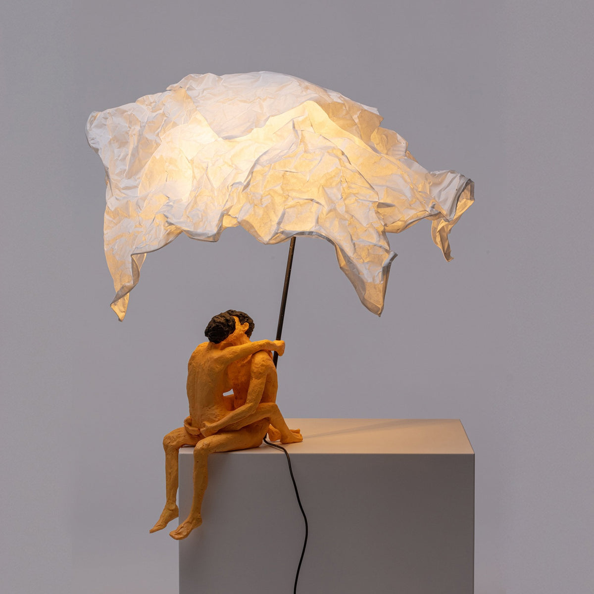 A modern art lamp with a couple embracing under a white crumpled shade, casting a warm glow.