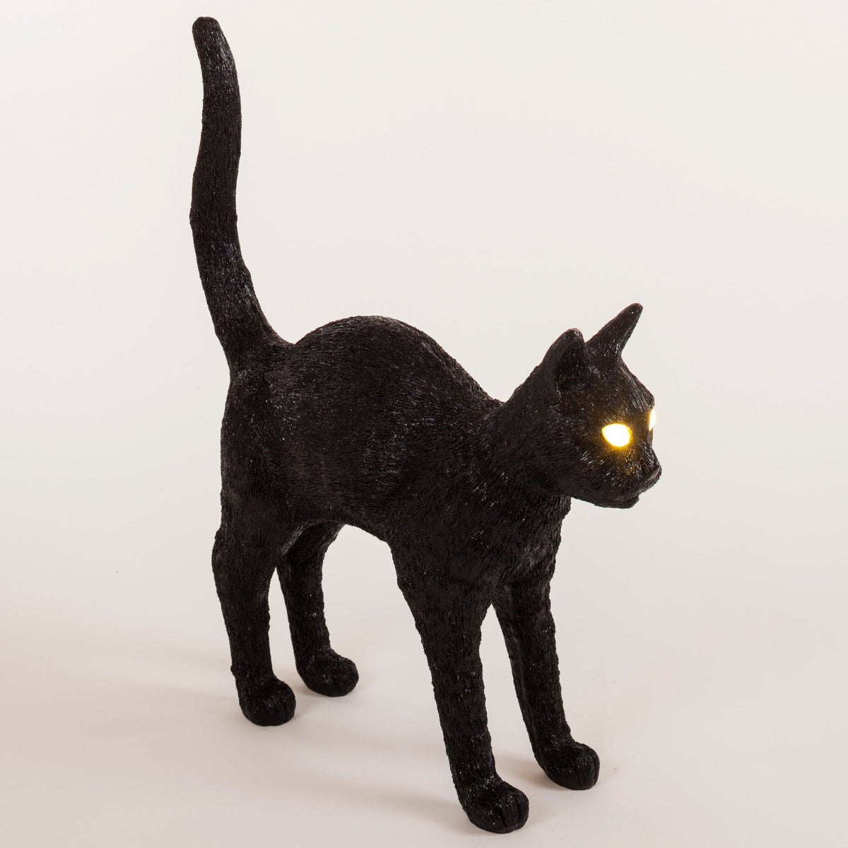 Black cat with luminous yellow eyes, arched back, and tail raised in an alert pose.