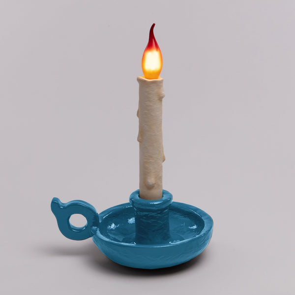 A flickering LED candle in a bright blue ceramic holder, set against a grey background.