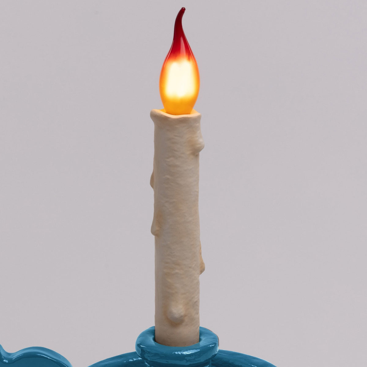 Close-up of the flickering LED candle and the top of its blue holder, on grey.