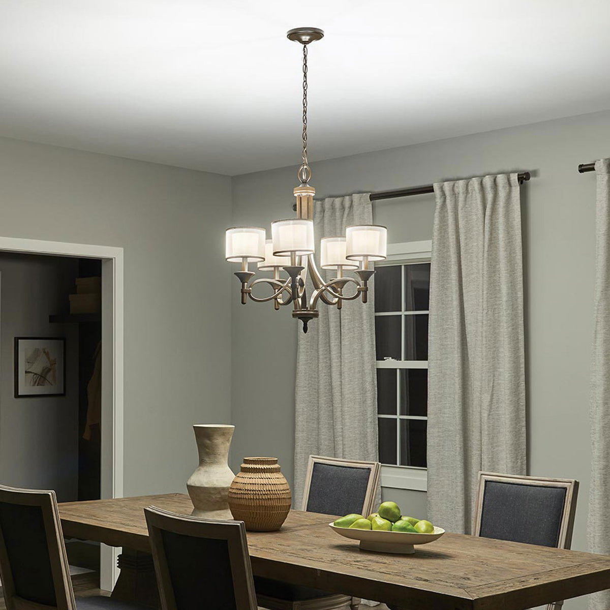 A dining room featuring a dark bronze chandelier with five drum shades at night.