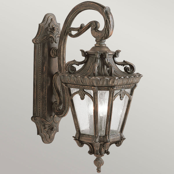 A close-up of a bronze outdoor wall light with a decorative arm and textured glass panels.