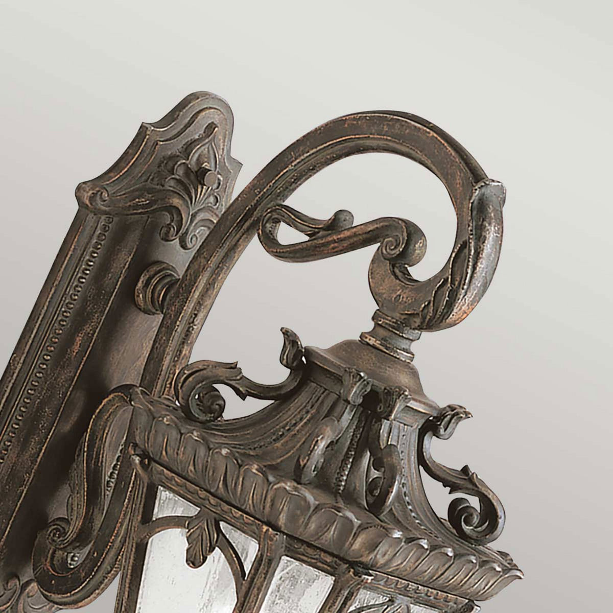 A detailed shot of the curved arm and decorative top of a bronze outdoor wall light.