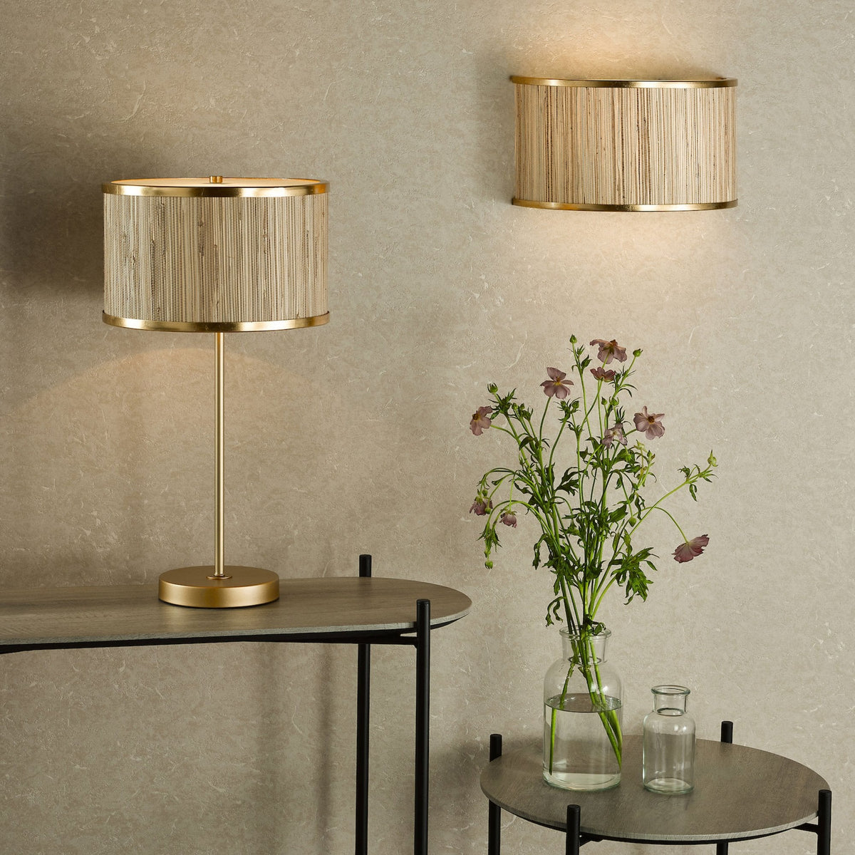 Table lamp and wall sconce with woven shades, next to a vase of flowers on a round table.