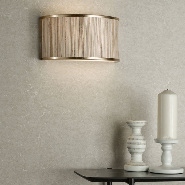 Textured wall with a gold and woven sconce, a white candle, and a decorative white holder on a dark table.