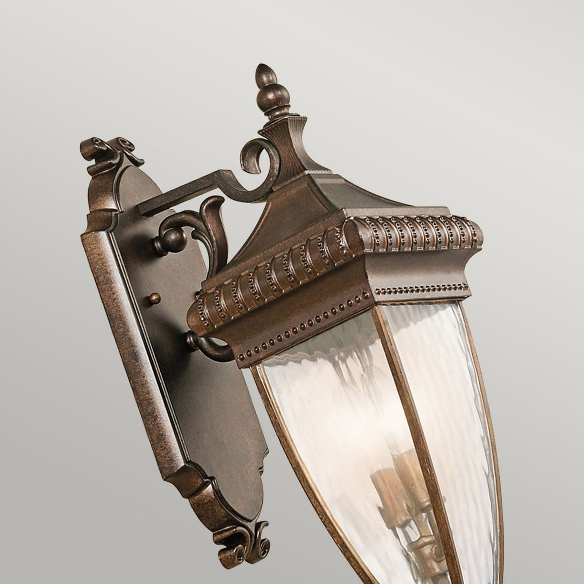 An ornate bronze outdoor wall light with fluted glass, viewed from an angle.