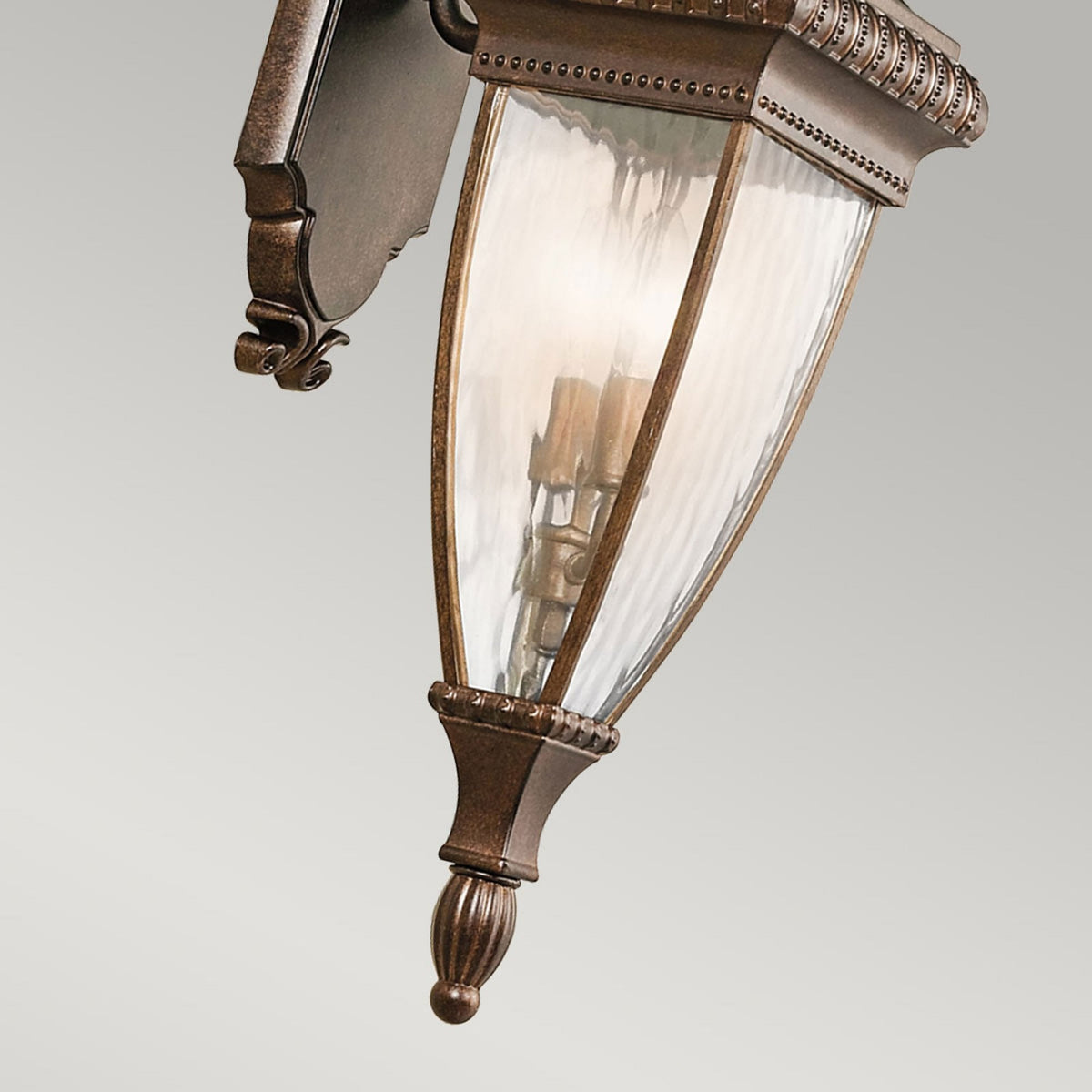 The bottom half of an ornate bronze outdoor wall light with fluted glass.