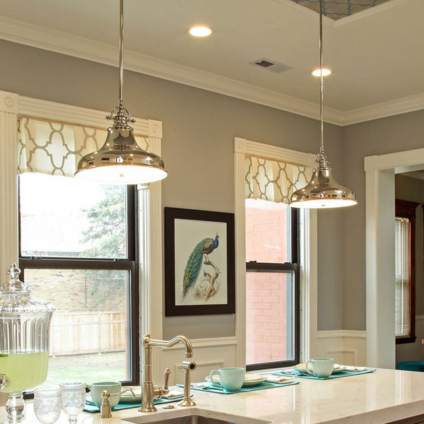 Two polished nickel pendant lights hanging above a kitchen island with place settings.
