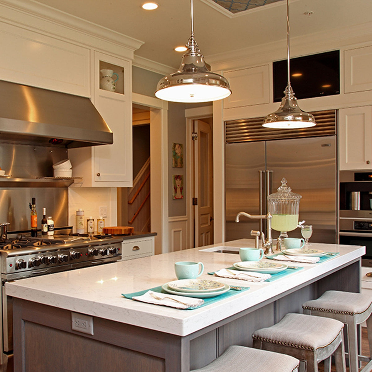 Polished nickel pendant lights illuminate a modern kitchen island with bar stools.