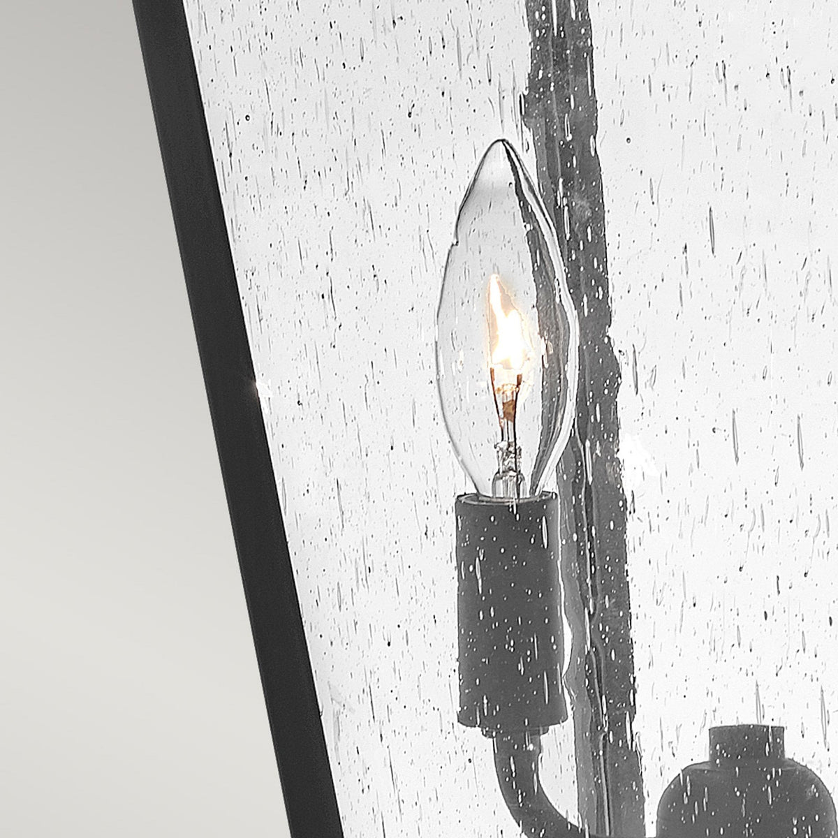 Close-up of a candelabra bulb within a seeded glass panel on an outdoor post light.