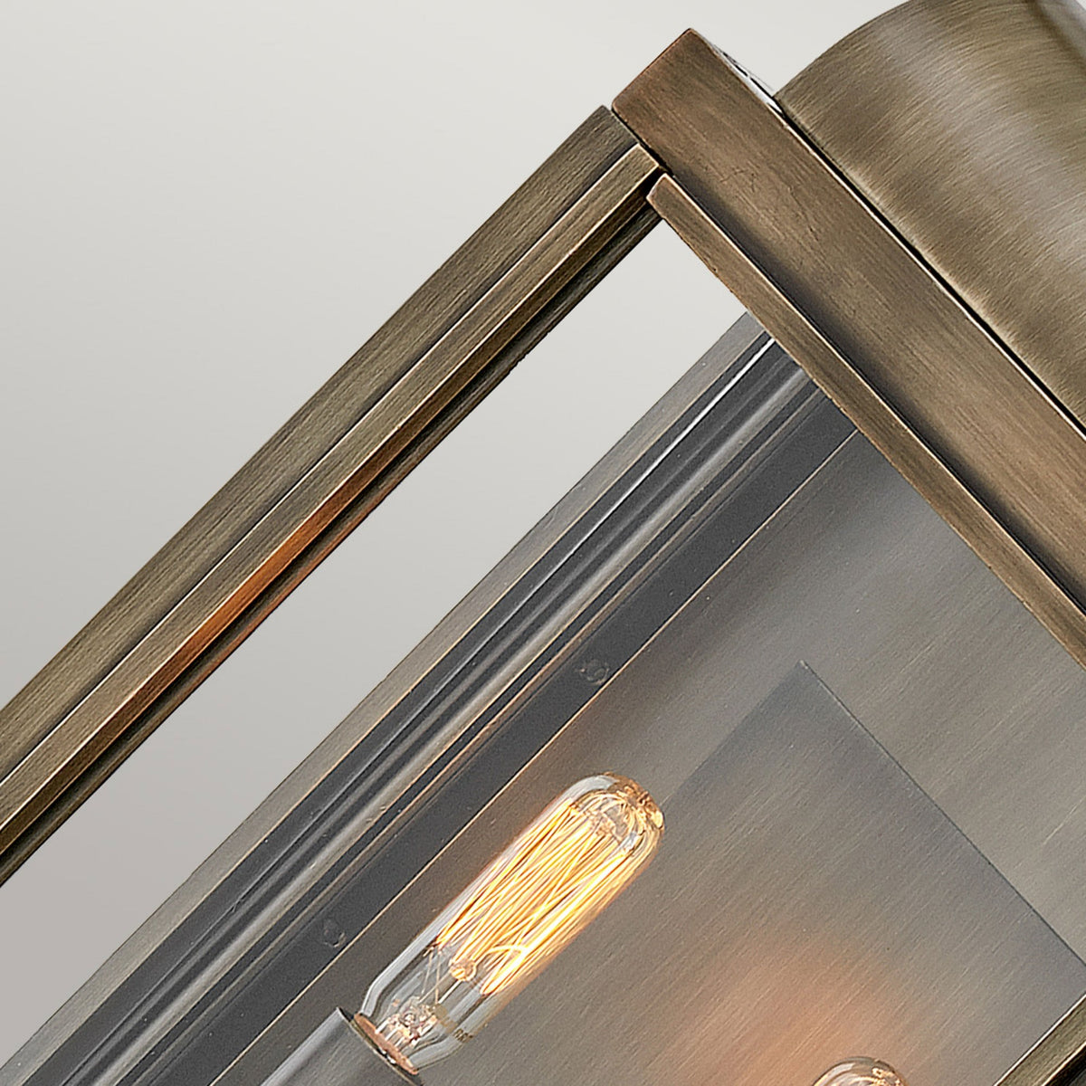 A close-up of a single exposed filament bulb within a brass outdoor lantern.