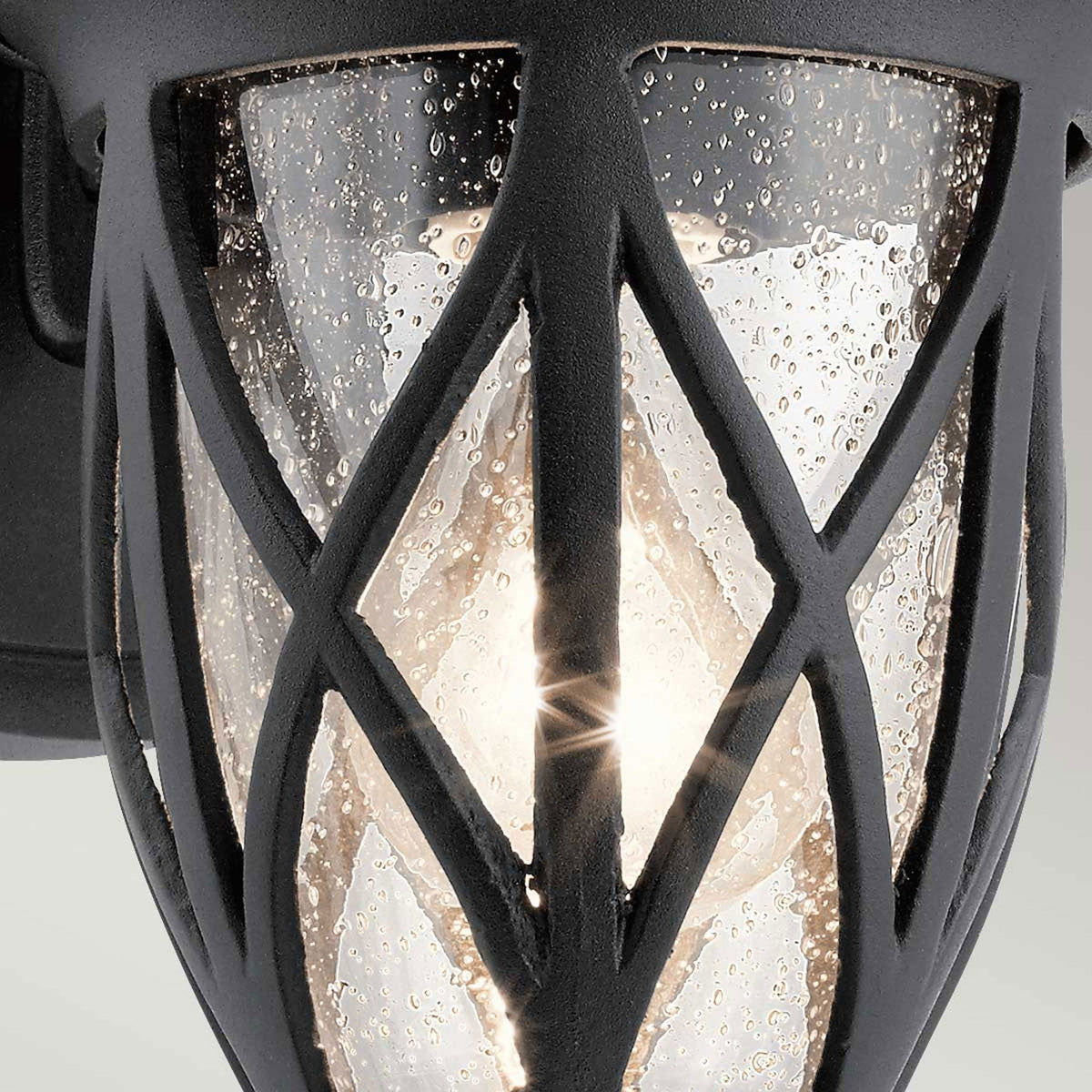 Close-up of the seeded glass and metalwork on a traditional black outdoor wall light.