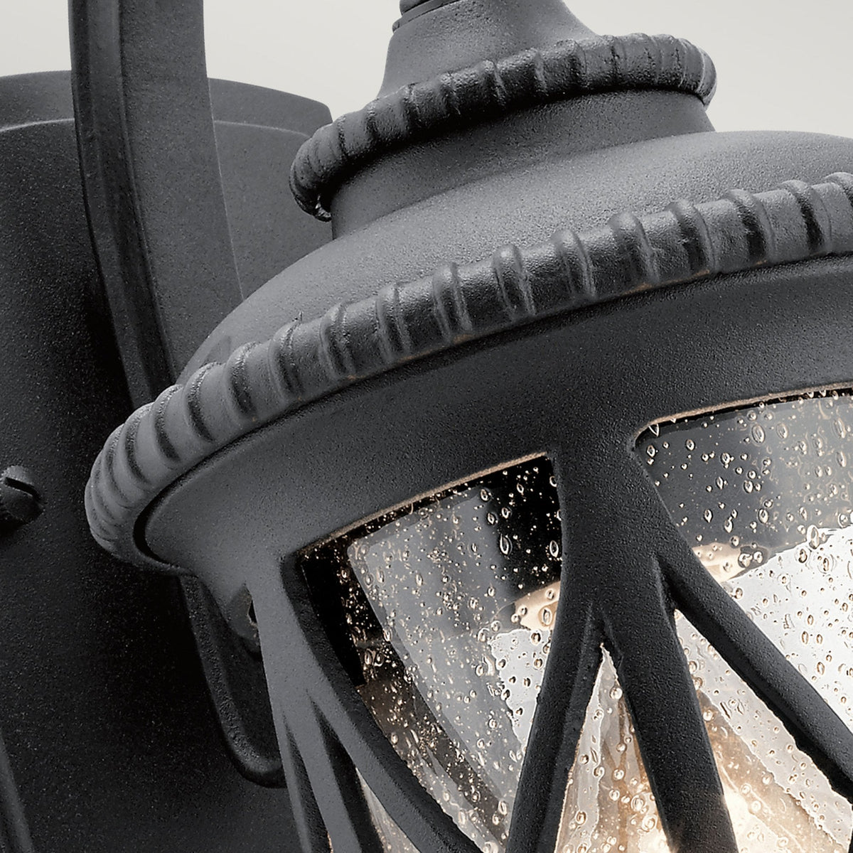 Detailed view of the top and glass texture of a traditional black outdoor wall light.