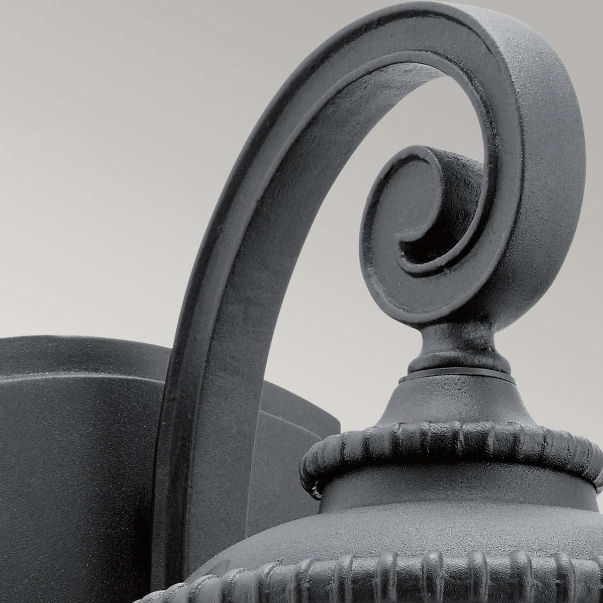 Close-up of the ornate scroll arm of a traditional black outdoor wall light.