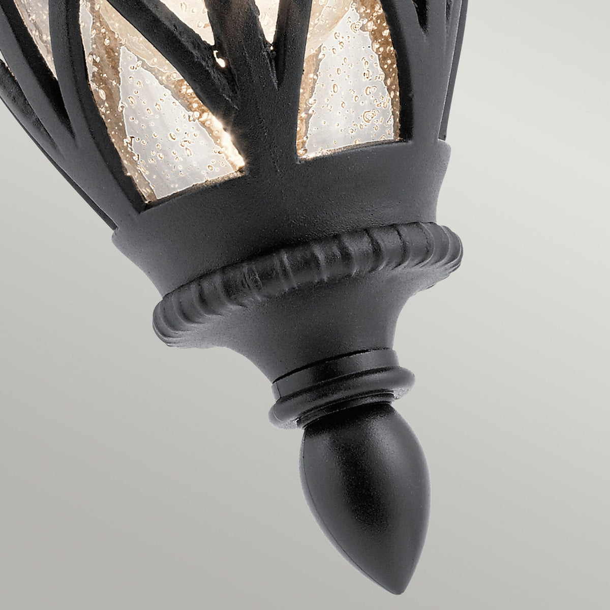 Detailed view of the finial and textured glass on a traditional black outdoor wall light.