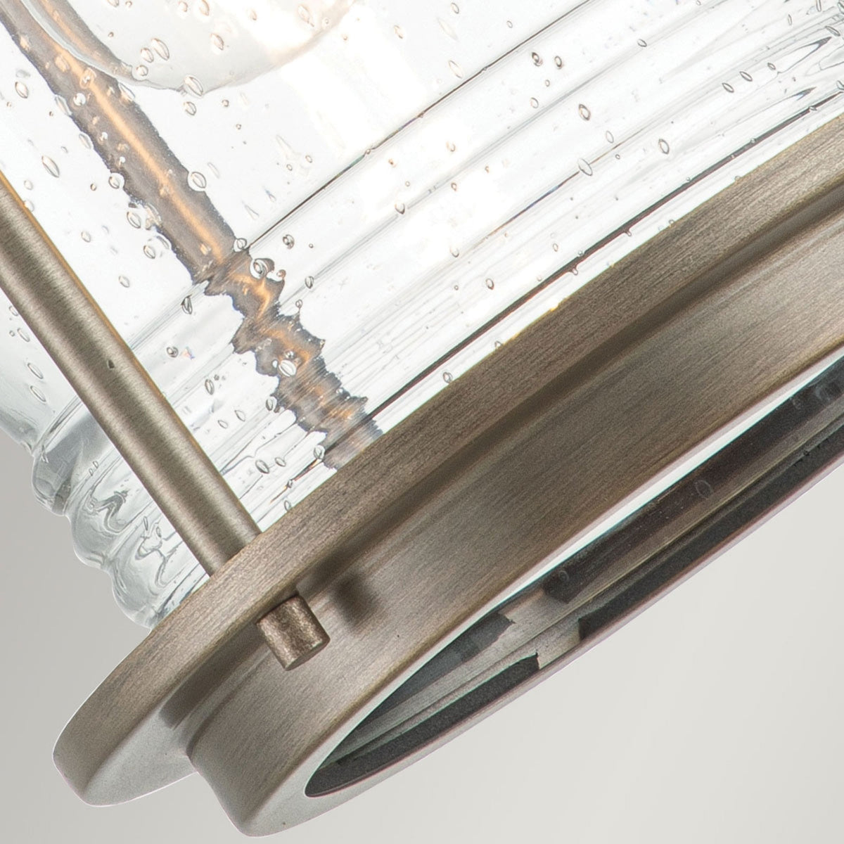 A close-up of the base of a bronze outdoor lantern, highlighting the seeded glass.