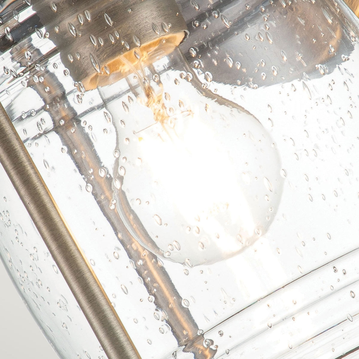 A close-up of the light bulb inside a bronze outdoor lantern with seeded glass.