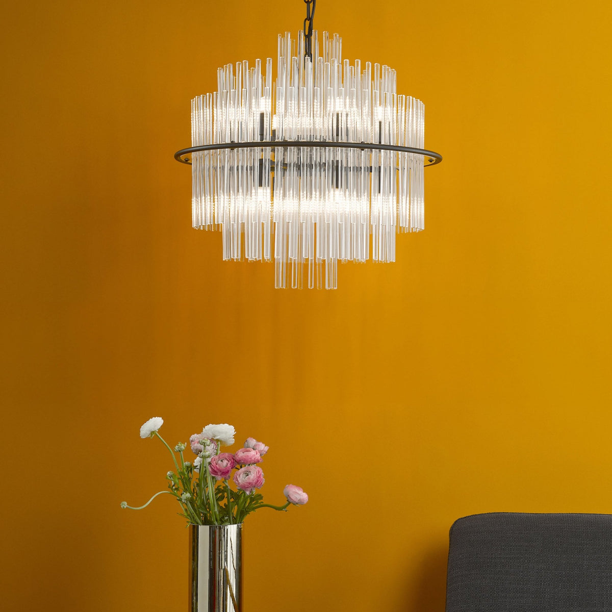 Modern chandelier with clear glass rods and a black frame, illuminating a vibrant yellow wall.