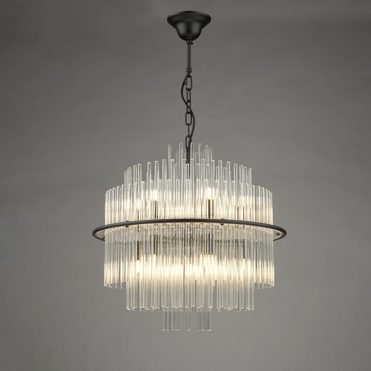 A modern chandelier with multiple clear glass rods arranged in a circular, tiered design, emitting a warm glow.
