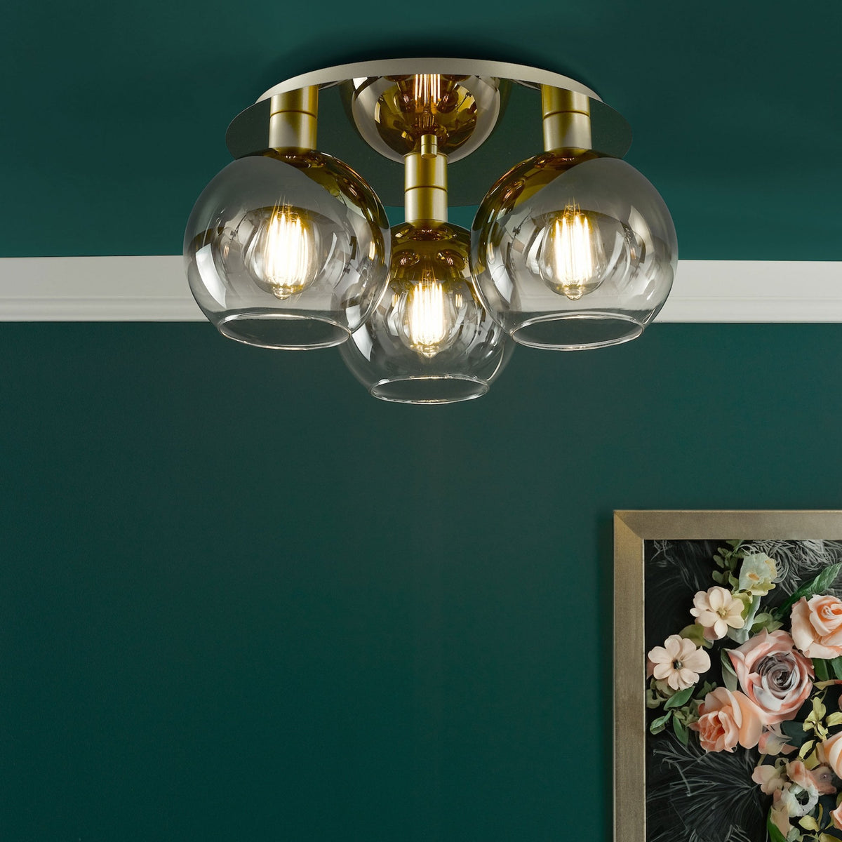 Three-light semi-flush mount ceiling fixture with clear glass globes and brass accents against a dark green ceiling.