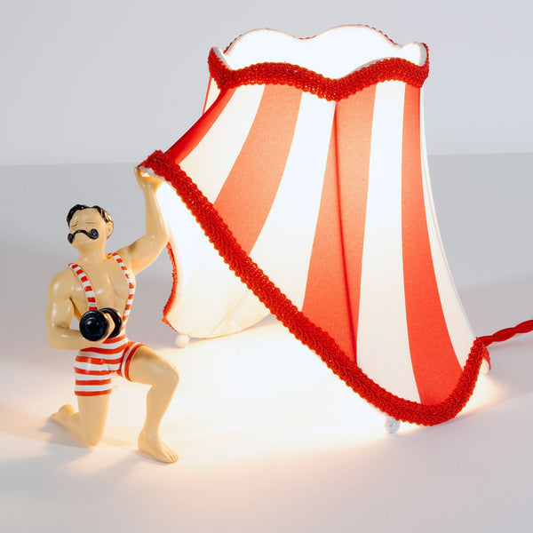 A circus strongman holding up a red and white striped lampshade with one hand.
