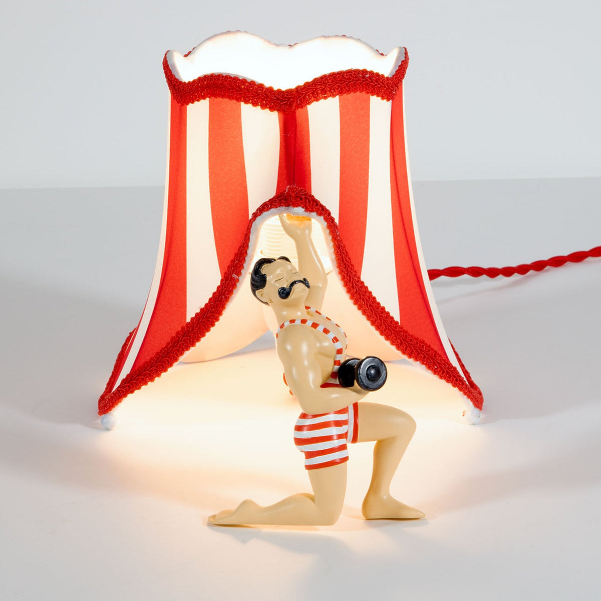 A circus strongman holding up a red and white striped lampshade from the back.