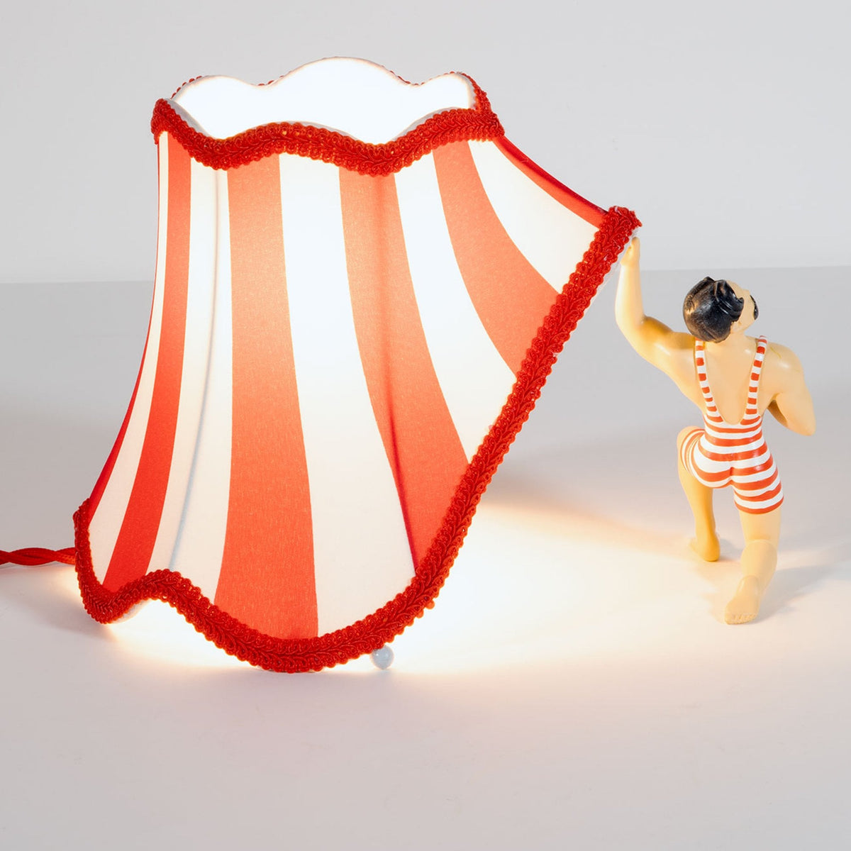A circus strongman from behind, holding up a red and white striped lampshade.