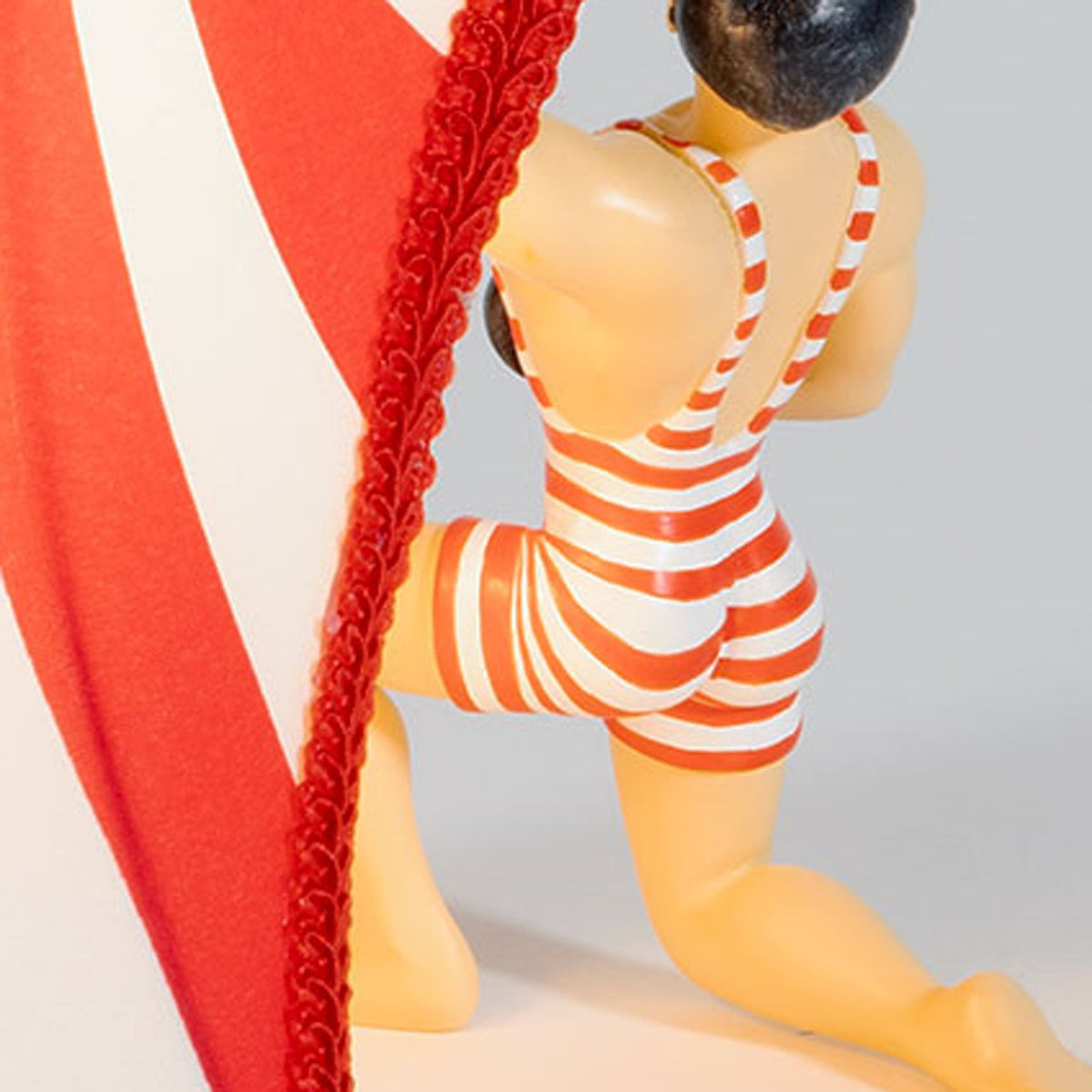 Close-up of the circus strongman's back and striped shorts, holding the lampshade.