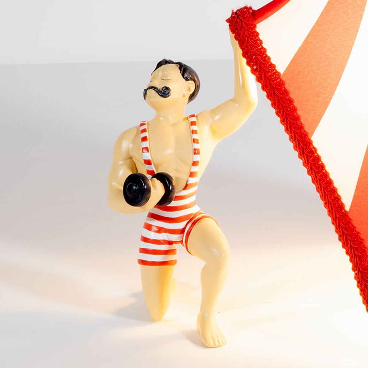 Close-up of the circus strongman's face and arm, holding up the lampshade.